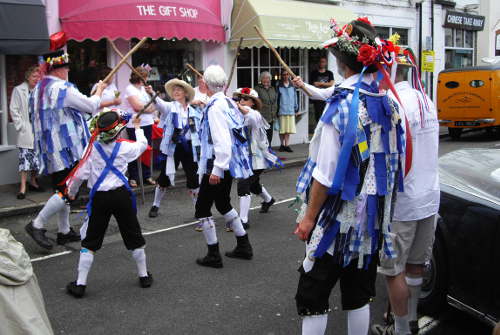 Morris dancers in white and blue uniforms dancing in a street